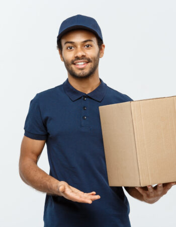 Delivery Concept - Portrait of Happy African American delivery man pointing hand to present a box package. Isolated on Grey studio Background. Copy Space.